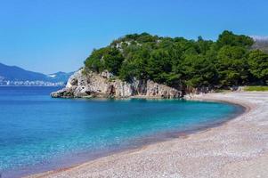 mar azul mediterráneo, playa con pequeños guijarros naranjas, rocas con pinos verdes. foto