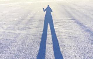 female shadow with long legs and a raised hand on fresh snow on a winter sunny day. Abstract photo