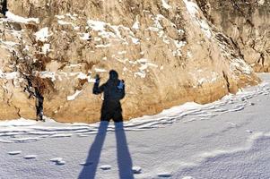 female shadow with long legs and a raised hand on fresh snow and a rock on a winter sunny day. Abstract photo