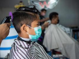 Teenage boy in a face protective mask is getting a haircut from a barbershop. Fashionable elongated haircuts for boys. Beauty salon in quarantine coronavirus covid-1 photo