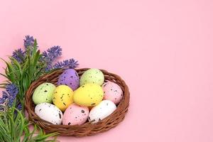 colorful Easter eggs in a basket on a pink background with lavender flowers, space for text photo