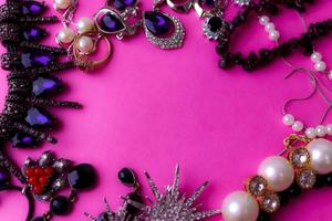 hermosas y preciosas joyas brillantes, joyas glamorosas de moda, collares, aretes, anillos, cadenas, broches con perlas y diamantes sobre un fondo rosa púrpura. endecha plana, vista superior, lugar de copia foto