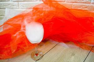 copa de vino con vapor sobre un fondo de tela roja y blanca y pared de ladrillo blanco. un vaso lleno de humo. foto