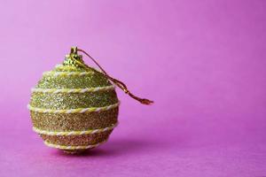 Golden yellow small round glass plastic winter smart shiny decorative beautiful xmas festive Christmas ball, Christmas toy pasted over with spangles on a violet pink background