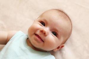 retrato de un lindo bebé sonriente con traje azul sobre una manta beige. foto