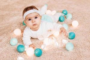 Cute little girl in blue and white dress is playing with Christmas lights on a beige plush plaid. photo