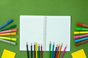 Felt tip pens, colored pencils and note for drawing. Stationery on green background. Concept back to school, education. Copy space photo