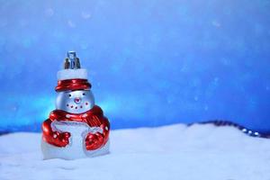 Snowman with a red scarf in the snow and blue sky from behind. Blurred background. Merry Christmas card. New year bokeh. Copy space photo