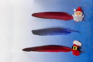 Gold, red, blue, silver feathers with pin with santa claus and a boot on a blue background. For list, write text, planning. Three lines. Christmas and New year photo