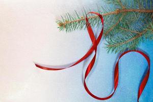 rama de abeto con cinta de raso rojo sobre fondo blanco-azul. tarjeta de navidad y año nuevo foto