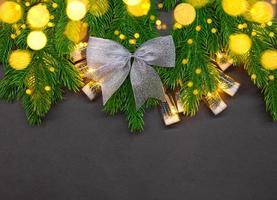 Silver bow on fir branches with bulbs and defocused light on black background with place for text. Christmas, New Year. Copy space photo