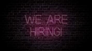 We are hirig text neon led sign animation. Vacancy job employment advertisement banner. Brick wall background video