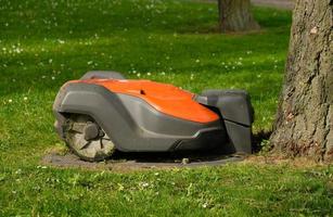 Robotic Lawn Mower on green grass background.Automatic robot lawnmower in modern garden.Green grass trimming with lawn mower. Close-up view of the lawn mower dirty blade after mowing the lawn. photo