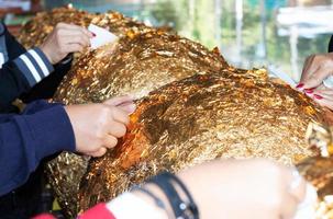 hands of buddhist gilding gold leaflet on golden ball in temple photo