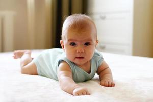 Cute little girl is lying on a bed and trying to crawl. photo