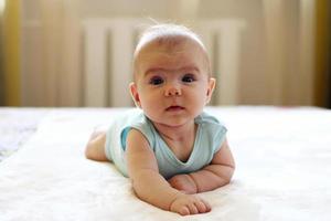 Little cute baby girl is trying to crawl on a bed at home. photo