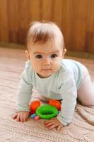 la niña está sentada en una tela escocesa de punto beige y jugando con un juguete de colores brillantes. foto