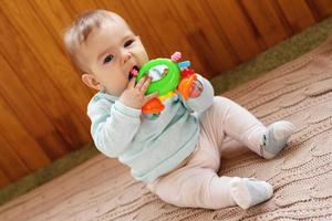 Beautiful little girl is sitting on a beige knitted plaid and playing with bright colorful toy. photo