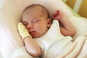 Cute newborn baby with yellow mitten on a hand is sleeping on her bed under beige blanket. photo