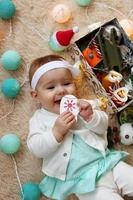 Cute little girl in blue and white dress is playing with wooden toy on a beige plaid with Christmas decorations and lights, top view. photo