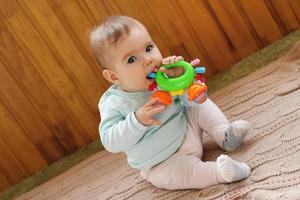 Beautiful little girl is sitting on a beige knitted plaid and playing with bright colorful toy. photo