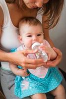 Mother helps her daughter to drink water. Child learns to hold a bottle. photo