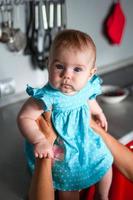 retrato sincero de una niñita vestida de azul sentada en la mesa de la cocina en manos de las madres. foto