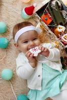 hermosa niña sonriente con vestido azul y blanco está jugando con un juguete de madera en una manta beige con decoraciones y luces navideñas, vista superior. foto