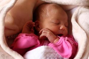 Cute sleeping newborn baby in pink baud on her bed under beige blanket. photo