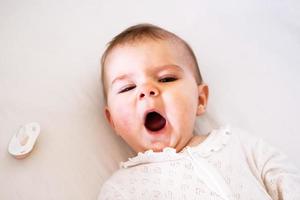 Adorable little baby girl is yawning on her bed before go to sleep. photo