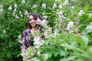 Portrait of beautiful young woman in black-purple dress in a garden with blooming lilac bushes. photo