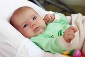 Cute infant little girl is lying in her bed under beige plaid. photo