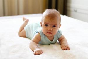 Cute little girl is lying on a bed and trying to crawl. photo