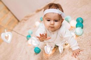 Curious little girl in blue and white dress is playing with wire of electricity Christmas lights. photo