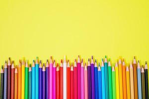 Assortment of colored pencils in various iridescent colors on a yellow photo