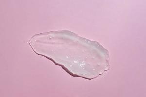 frotis de gel líquido sobre fondo rosa. manchas cosméticas de belleza como aloe transparente puro o loción de caracol, suero de gelatina facial, limpiador, gel de ducha o vista superior de champú. foto