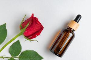 Dark glass bottle of cosmetic liquid and rose flower. Dropper bottle, hyaluronic acid, oil, serum, skin care product. Top view, mockup photo