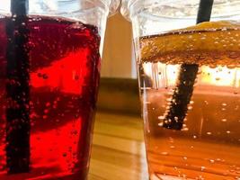 Two glasses of plastic red and yellow refreshing cold tasty sweet raspberry strawberry cherry orange peach lemon fruit lemonade natural with a straw and syrup bubbles photo