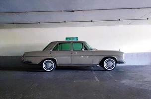 Bangkok, Thailand - June 20, 2022 Brown Mercedes Benz parked in parking with white concrete wall background. Vintage or retro car on street. Classic vehicle on road produces from England and luxury. photo