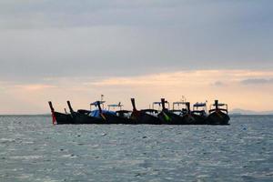 botes de cola larga flotando o estacionándose en el mar con olas y cielo al atardecer o al amanecer en krabi, tailandia. belleza en la naturaleza, transporte y viaje el día de vacaciones. vista del paisaje de belleza. foto