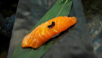 cierra el sushi de salmón fresco en la hoja de bambú verde en el restaurante japonés. comida asiática, delicioso pescado rebanado en arroz japonés con espacio para copiar. concepto de estilo de vida de alimentación saludable. foto