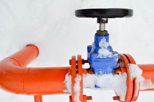 Industrial shut-off regulating protective pipe fittings. Black valve for opening, closing on an iron orange metal pipe with flanges, studs, nuts against the background of white snow in winter photo