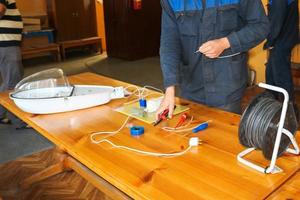 un electricista que trabaja, recoge el circuito eléctrico de una gran farola blanca con cables, un relé en una fábrica de plantas industriales foto