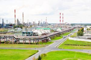 paisaje industrial. vista panorámica de las tuberías tecnológicas. ajustes de la planta. de las tuberías químicas rojo-blancas sale humo. edificios de producción. contra el fondo del cielo y la hierba brillante foto