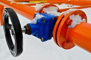 Industrial shut-off regulating protective pipe fittings. Black valve for opening, closing on an iron orange metal pipe with flanges, studs, nuts against the background of white snow in winter photo