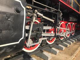 grandes ruedas de hierro de un tren rojo y negro parado sobre rieles y elementos de suspensión con resortes de una vieja locomotora de vapor industrial foto