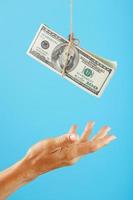 A wad of dollars on a string above a human palm on a blue background. photo