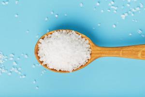 Sea salt in a wooden spoon on a blue background, with scattered salt. photo