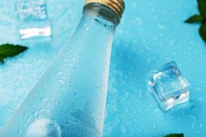 Cold Water Bottle, ice cubes, drops and mint leaves on a blue background. photo