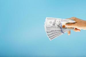 A hand with one hundred-dollar bills on a blue background. photo